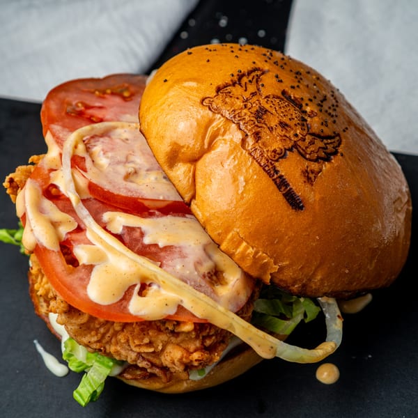 A crispy chicken burger from Little Angel Burgers & Wings, with lettuce, tomato, and sauce.