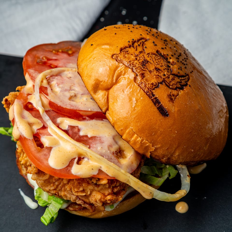 A crispy chicken burger from Little Angel Burgers & Wings, with lettuce, tomato, and sauce.