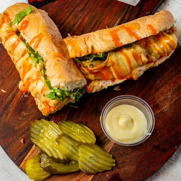Two halves of a cheesy, saucy sub sandwich with lettuce, pickles, and a side of mayo.