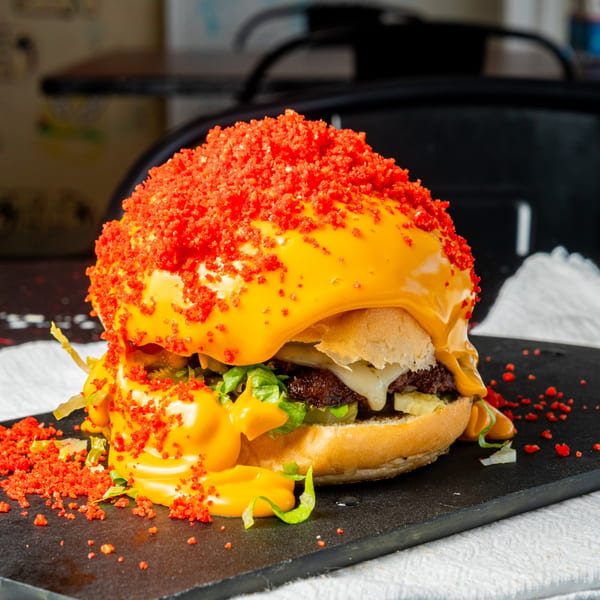 A Little Angel Burgers & Wings burger, drenched in cheese sauce and topped with red crunchy bits.