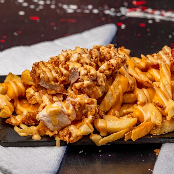 Crispy chicken pieces and golden fries generously drizzled with creamy cheese sauce on a dark platter.
