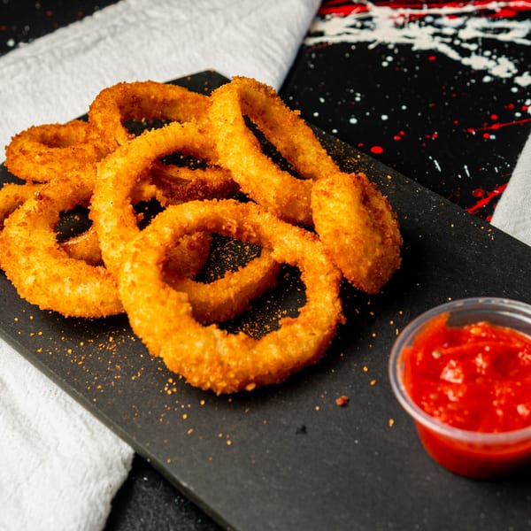 Golden-brown, crispy onion rings from Little Angel Burgers & Wings, served with a side of red dipping sauce.