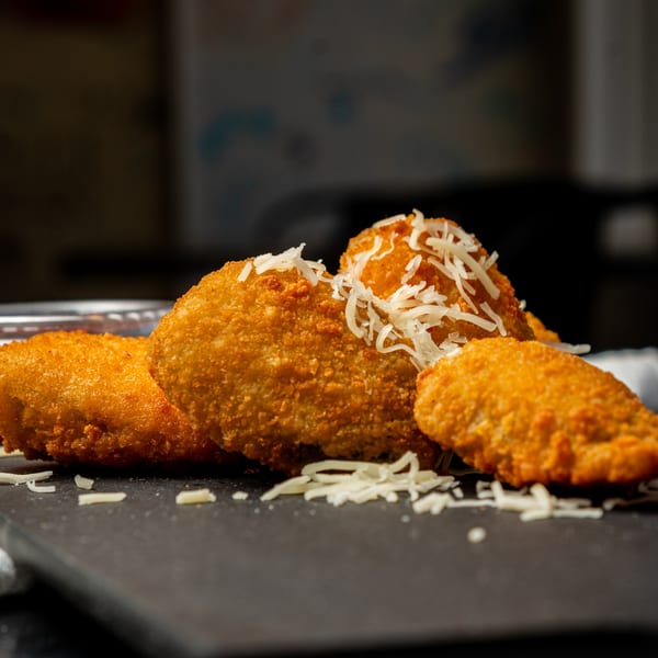 Golden-brown fried chicken pieces, some topped with shredded white cheese, on a dark serving board.